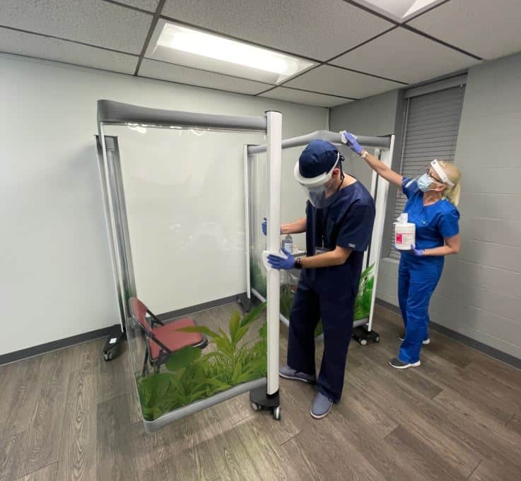 Staff wiping down a Rolascreen partition with hospital-grade disinfectant — wipe-in-place cleaning workflow